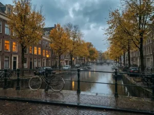 Bicycle leaning on a rain-slicked cobblestone bridge along a misty Dutch canal lined with golden autumn trees and brick rowhouses.