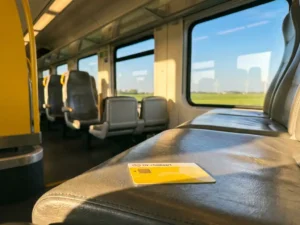 Yellow OV-chipkaart on a train seat in a sunlit Dutch intercity carriage with polder landscape visible through windows.